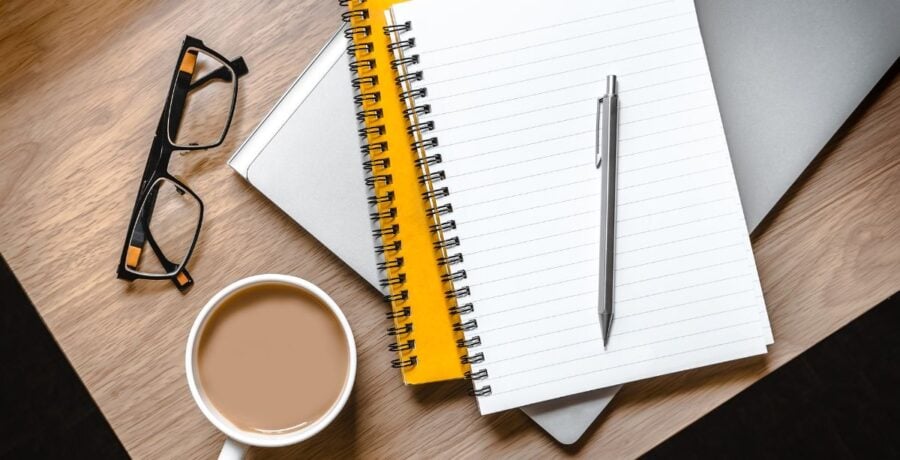 Pile of notepads on desk with glasses and a cup of tea